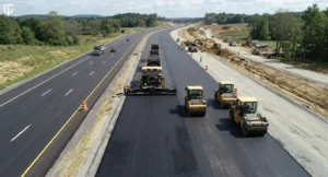 Asphalt concrete road being paved and compacted with an asphalt paver and rollers.